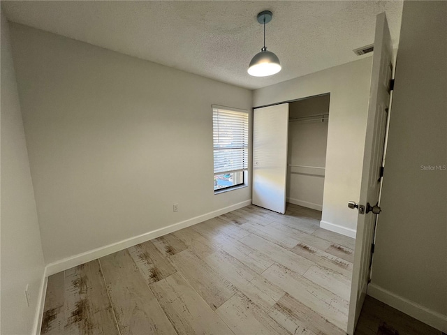 unfurnished bedroom featuring a closet, a textured ceiling, and light wood-type flooring