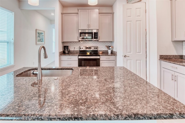 kitchen with stainless steel appliances, sink, backsplash, and dark stone counters