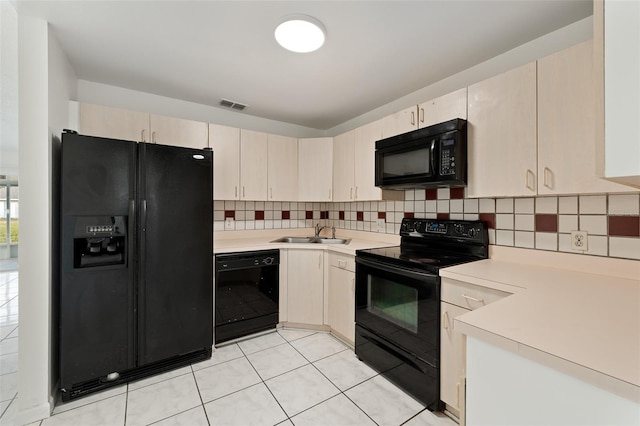 kitchen with sink, backsplash, light tile patterned floors, black appliances, and cream cabinets