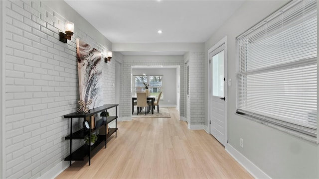 hallway featuring brick wall and light wood-type flooring