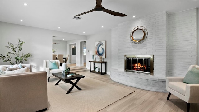 living room featuring ceiling fan, a fireplace, and light wood-type flooring