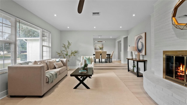 living room featuring ceiling fan, light hardwood / wood-style floors, and a brick fireplace