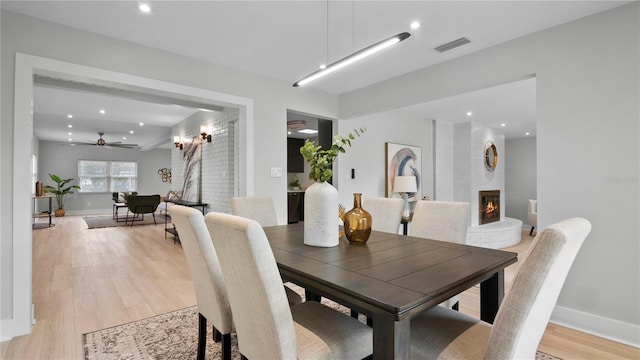 dining space with ceiling fan, a fireplace, and light hardwood / wood-style flooring