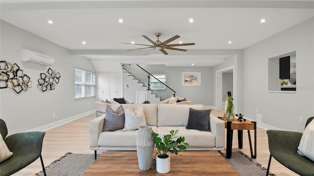 living room with beamed ceiling, a wall mounted AC, and light hardwood / wood-style flooring