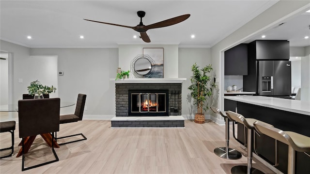 dining area featuring crown molding, ceiling fan, a fireplace, and light hardwood / wood-style flooring