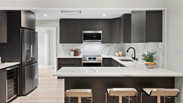 kitchen featuring wine cooler, sink, appliances with stainless steel finishes, a kitchen breakfast bar, and kitchen peninsula