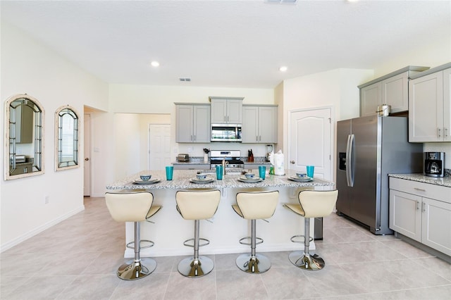 kitchen with light tile patterned floors, stainless steel appliances, and an island with sink