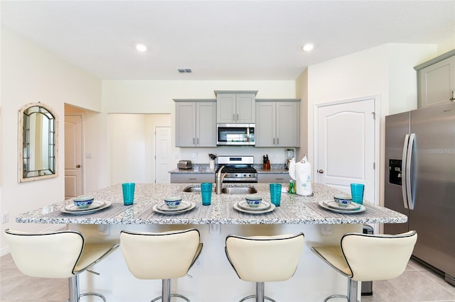 kitchen featuring sink, light tile patterned floors, a kitchen breakfast bar, stainless steel appliances, and a kitchen island with sink