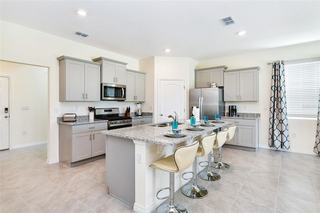 kitchen with gray cabinetry, stainless steel appliances, a kitchen breakfast bar, and an island with sink