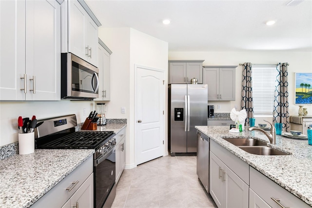 kitchen with sink, gray cabinetry, light stone counters, light tile patterned floors, and appliances with stainless steel finishes