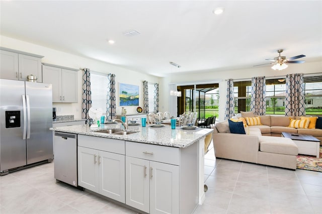 kitchen featuring light tile patterned flooring, sink, light stone counters, stainless steel appliances, and a kitchen island with sink