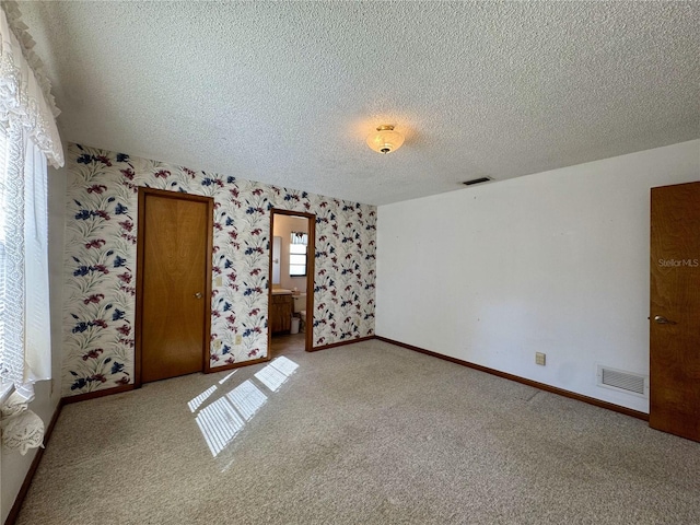 unfurnished bedroom featuring light carpet, a textured ceiling, and ensuite bathroom