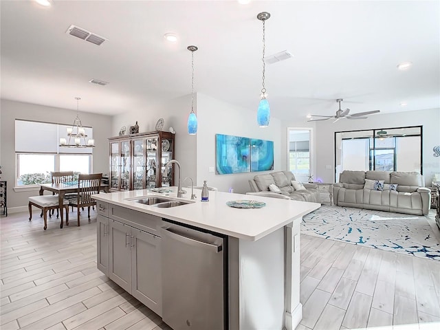 kitchen with pendant lighting, sink, gray cabinets, dishwasher, and an island with sink