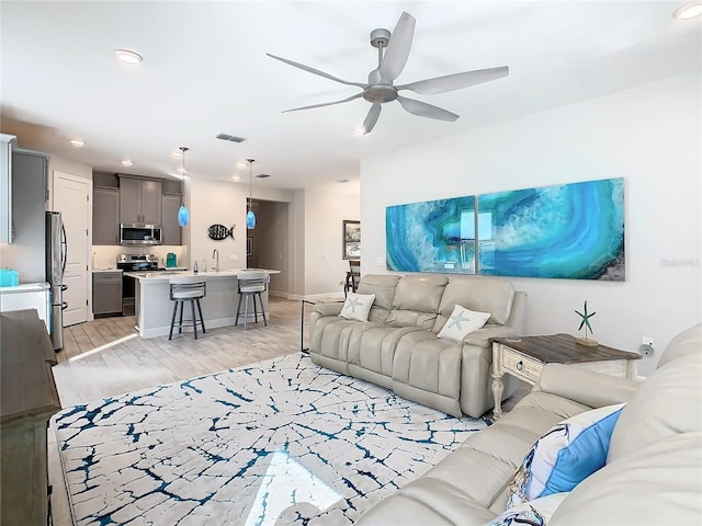 living room with sink, light hardwood / wood-style flooring, and ceiling fan