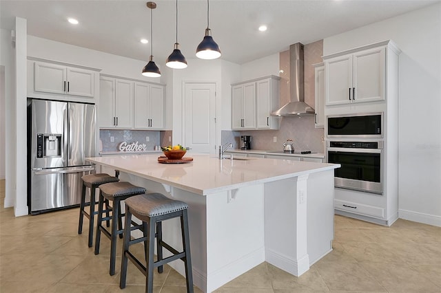 kitchen with white cabinetry, a kitchen bar, wall chimney range hood, stainless steel appliances, and a center island with sink