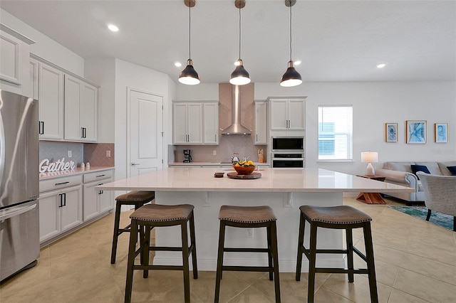 kitchen with appliances with stainless steel finishes, pendant lighting, decorative backsplash, a large island, and wall chimney exhaust hood