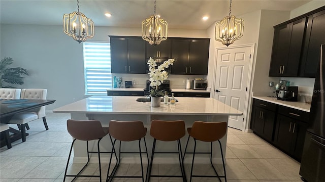 kitchen featuring sink, decorative light fixtures, a center island with sink, light tile patterned floors, and black refrigerator