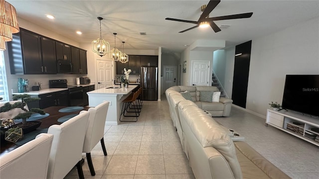 kitchen with sink, a kitchen breakfast bar, an island with sink, pendant lighting, and black appliances