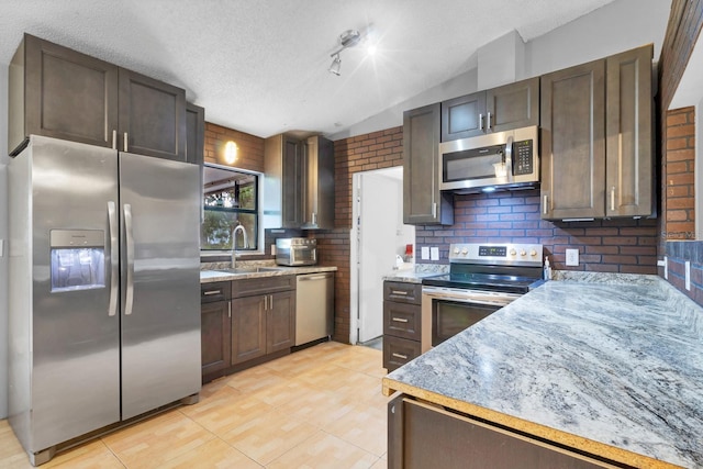 kitchen with dark brown cabinetry, sink, light stone counters, a textured ceiling, and stainless steel appliances