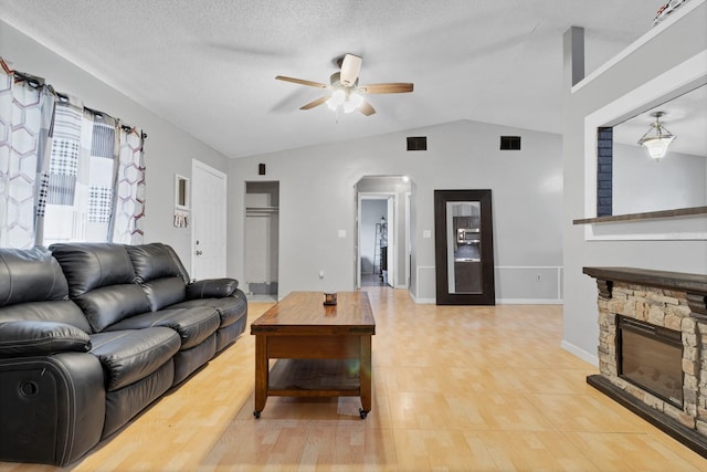 living room with ceiling fan, lofted ceiling, a fireplace, and a textured ceiling