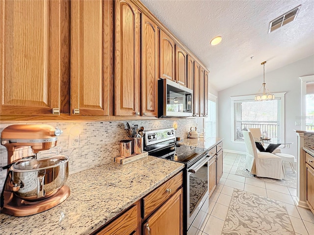 kitchen featuring light stone counters, vaulted ceiling, light tile patterned floors, stainless steel appliances, and backsplash