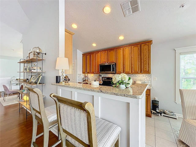 kitchen with light stone counters, a breakfast bar area, kitchen peninsula, and range