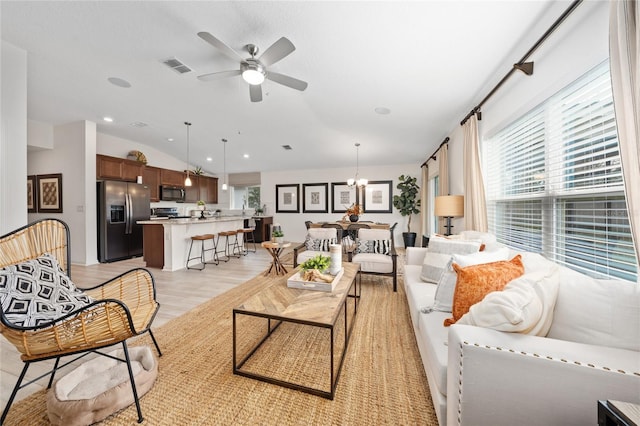 living room featuring lofted ceiling, light hardwood / wood-style floors, and ceiling fan with notable chandelier