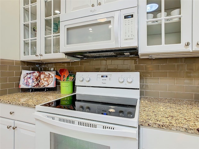 kitchen with light stone countertops, backsplash, white cabinets, and white appliances