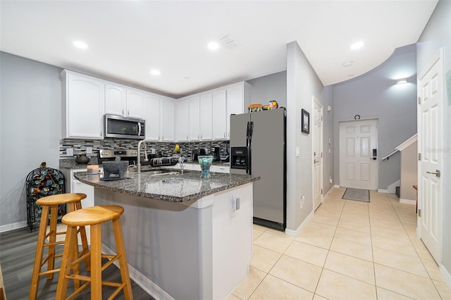 kitchen featuring a breakfast bar, an island with sink, white cabinets, dark stone counters, and stainless steel appliances