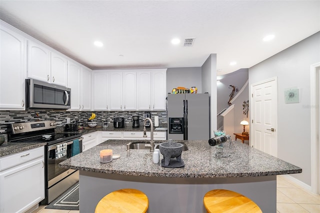 kitchen with a kitchen island with sink, dark stone countertops, and appliances with stainless steel finishes