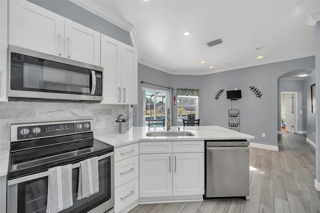 kitchen featuring appliances with stainless steel finishes, white cabinetry, sink, decorative backsplash, and ornamental molding