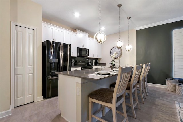 kitchen featuring white cabinetry, decorative light fixtures, a center island with sink, and black appliances