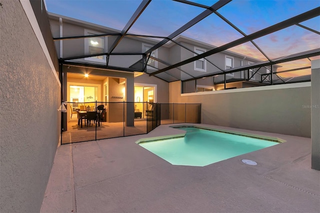 pool at dusk with glass enclosure and a patio