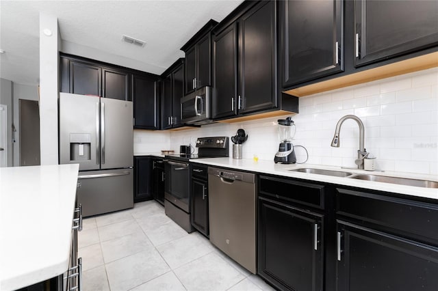 kitchen featuring light tile patterned flooring, sink, a textured ceiling, appliances with stainless steel finishes, and decorative backsplash