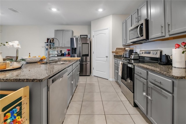 kitchen with light tile patterned flooring, stainless steel appliances, gray cabinets, and dark stone counters