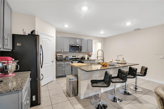 kitchen with sink, gray cabinets, a breakfast bar, appliances with stainless steel finishes, and a kitchen island with sink