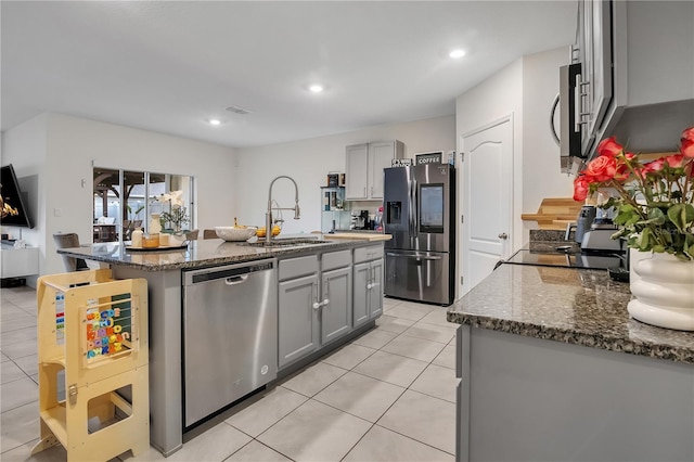 kitchen with sink, dark stone counters, gray cabinets, stainless steel appliances, and a kitchen island with sink