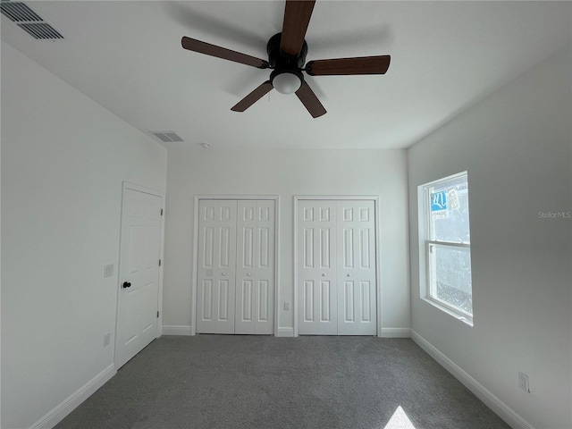 unfurnished bedroom with multiple closets, dark colored carpet, and ceiling fan