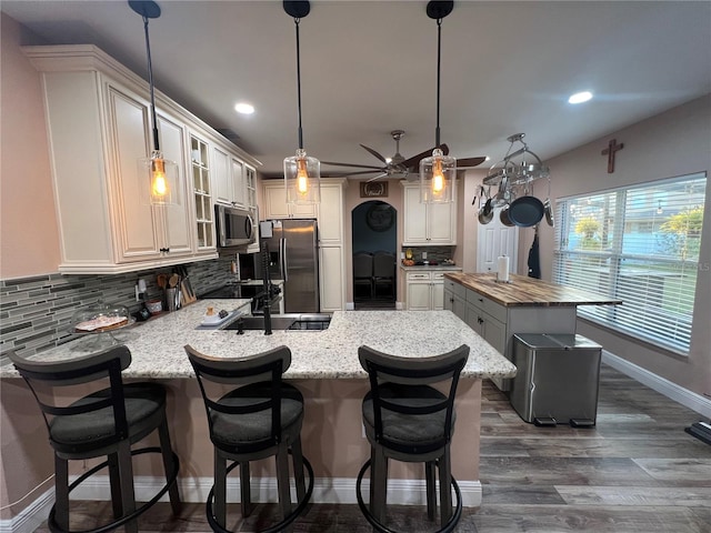 kitchen with decorative light fixtures, wooden counters, decorative backsplash, a kitchen island with sink, and stainless steel appliances