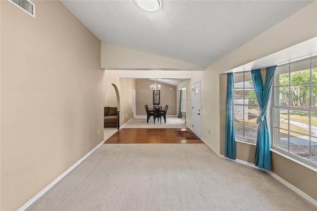 hall featuring lofted ceiling, carpet floors, a textured ceiling, and a notable chandelier