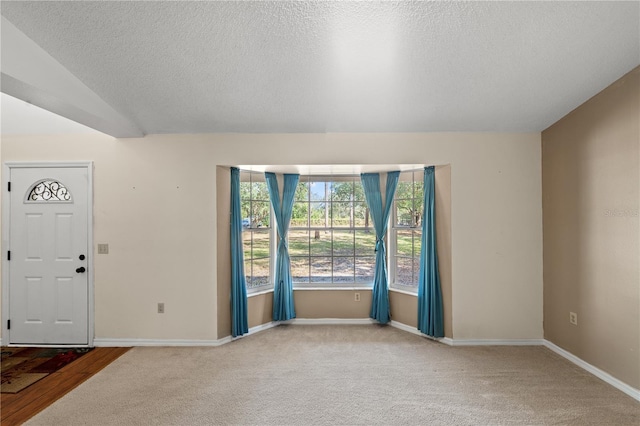 foyer featuring lofted ceiling, carpet, and a textured ceiling