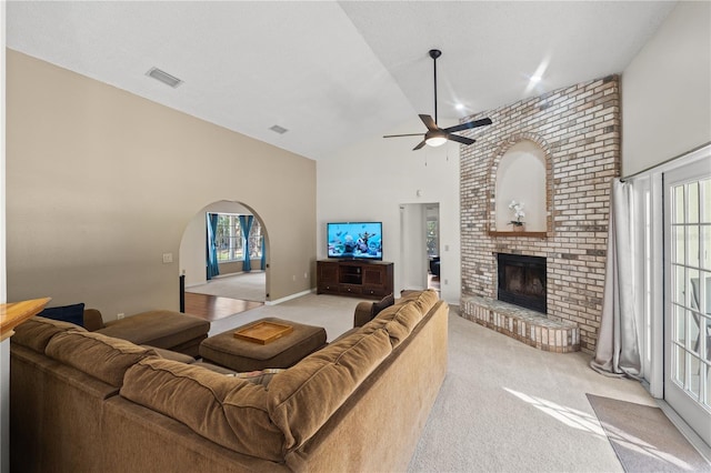 living room with ceiling fan, a brick fireplace, high vaulted ceiling, and light carpet