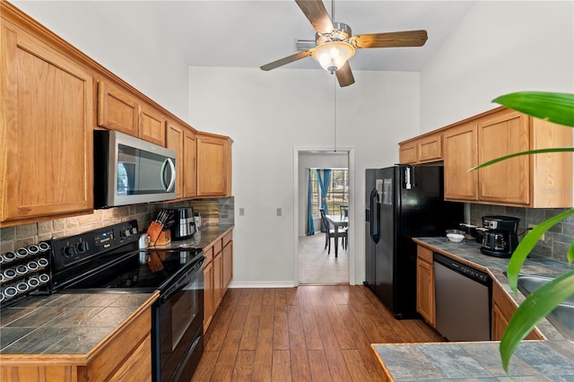 kitchen with black appliances, dark hardwood / wood-style floors, tile counters, a high ceiling, and backsplash