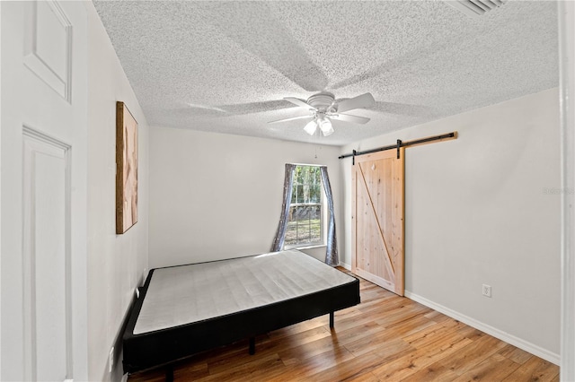 bedroom featuring ceiling fan, a barn door, a textured ceiling, and light hardwood / wood-style flooring