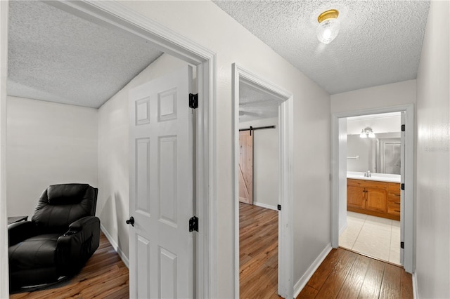 hallway with wood-type flooring, a barn door, sink, and a textured ceiling