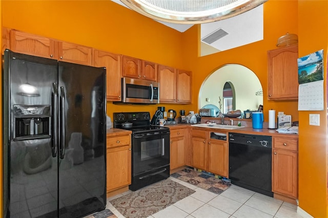 kitchen with sink, a towering ceiling, black appliances, and light tile patterned flooring