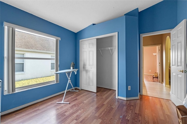 unfurnished bedroom with hardwood / wood-style flooring, vaulted ceiling, a closet, and a textured ceiling