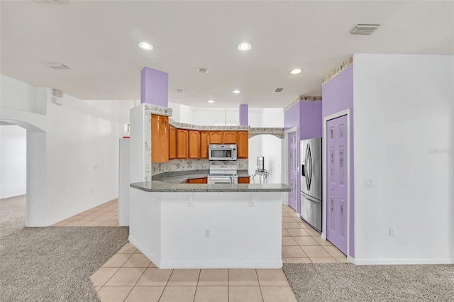 kitchen with stone countertops, light carpet, kitchen peninsula, stainless steel appliances, and decorative backsplash