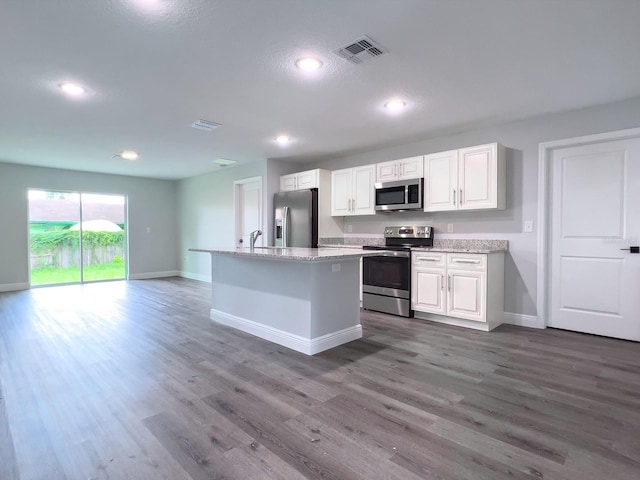 kitchen featuring white cabinetry, an island with sink, dark hardwood / wood-style flooring, light stone counters, and stainless steel appliances