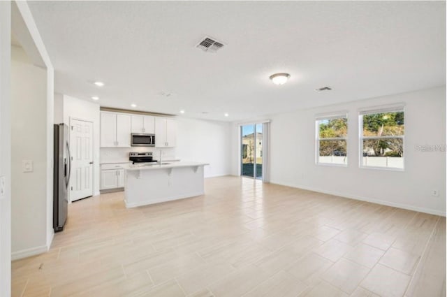 kitchen with white cabinetry, a breakfast bar, an island with sink, and appliances with stainless steel finishes